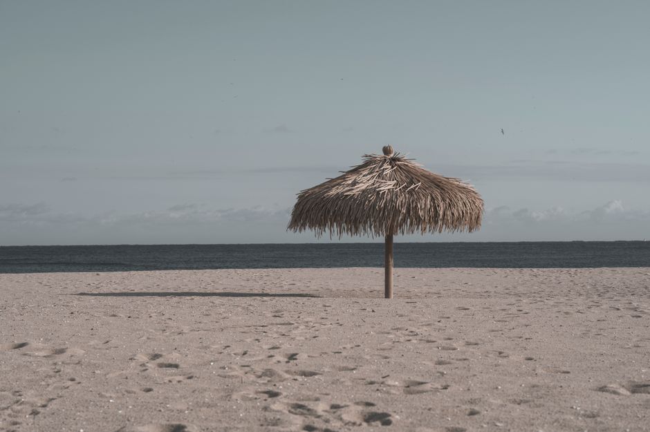 Peaceful sandy beach with a single straw umbrella under a blue sky and open ocean.