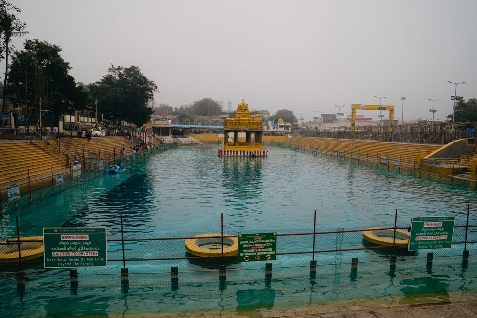 A serene view of the sacred tank at a famous Hindu temple in Tirupati, India, with devotees present.