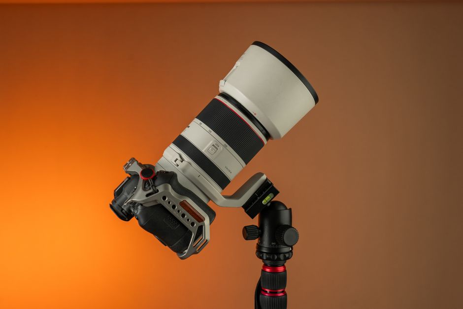 Close-up of a high-end telephoto camera lens mounted on a tripod against a warm background.