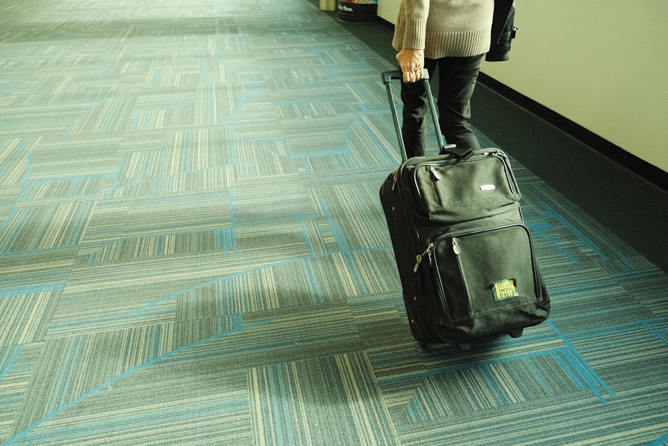 Person walking with luggage on blue carpeted airport corridor, traveling