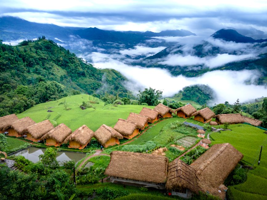 Aerial view of traditional huts surrounded by lush, misty mountains and nature.