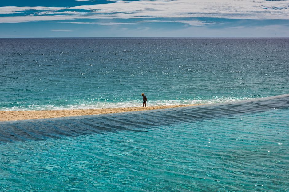 A lone person strolls along the serene beach in San José del Cabo, Mexico under a bright blue sky.