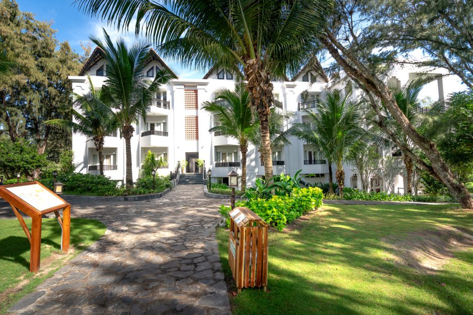 A pristine white hotel building surrounded by lush tropical gardens with palm trees under a clear blue sky.