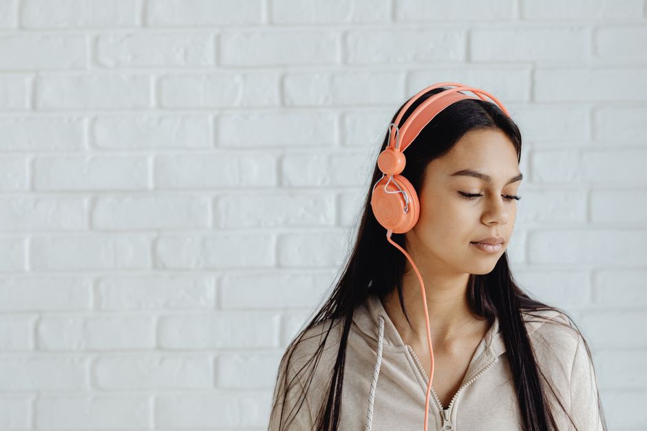 A serene young woman listens to music with headphones against a white brick wall.