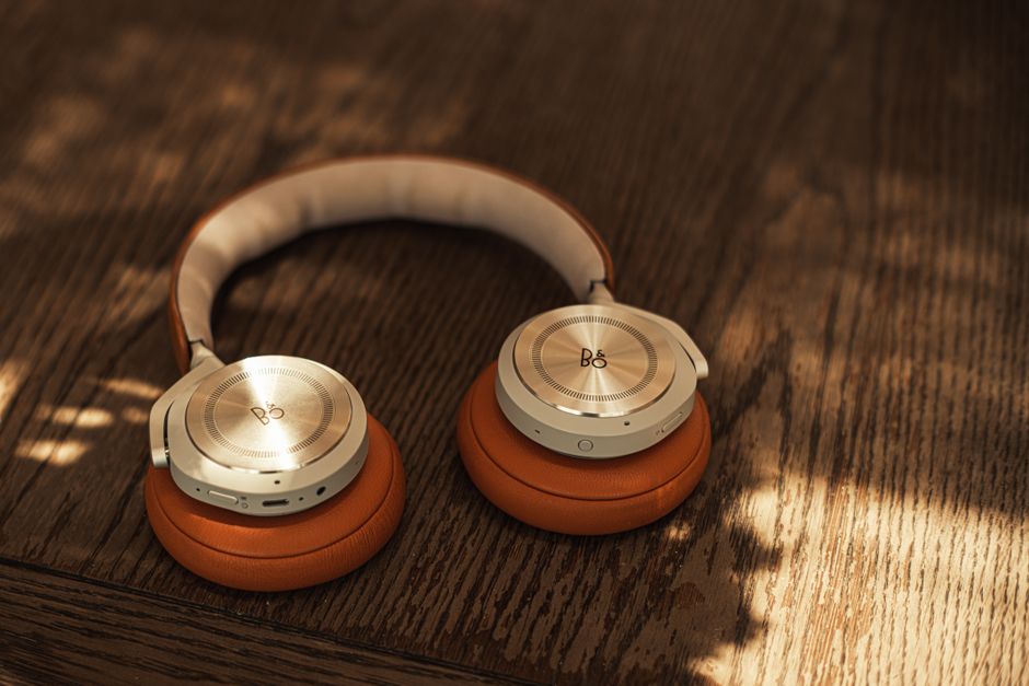 Stylish wireless headphones with orange cushions on a wooden surface, lit by natural light.