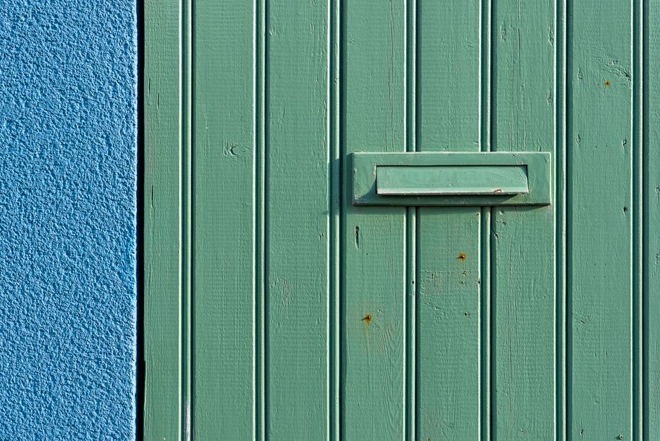 A textured green wooden door with a mail slot against a vibrant blue wall, featuring a striking color contrast.