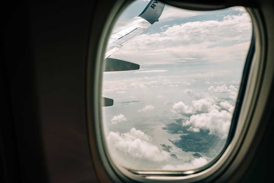 View through airplane window showing wing and ocean with clouds below during daylight flight.