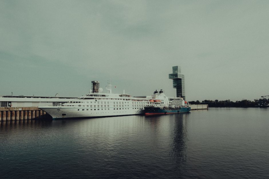 Two elegant cruise ships docked at a modern marina with contemporary architecture in the background.