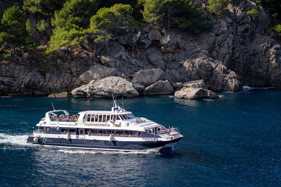 Panoramic view of a cruise ship sailing along a rocky coastline under clear blue skies.