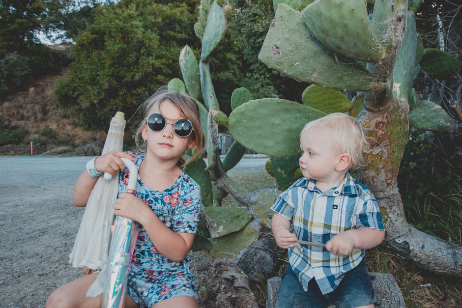 Two children sitting by a cactus in a park, enjoying a summer day.