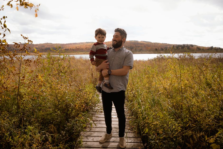 A father and son enjoying a walk in a lush fall setting near a lake, capturing a joyful family moment.
