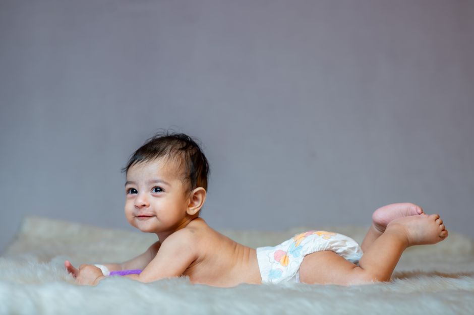 Happy baby in diaper lying on a soft blanket indoors, showcasing a joyful expression.