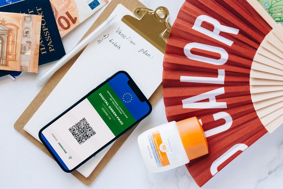 Flat lay of travel essentials featuring a digital green pass, passport, and other travel items on a table.