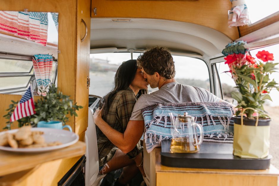 Couple enjoys a romantic moment kissing inside a cozy camper van during a road trip.