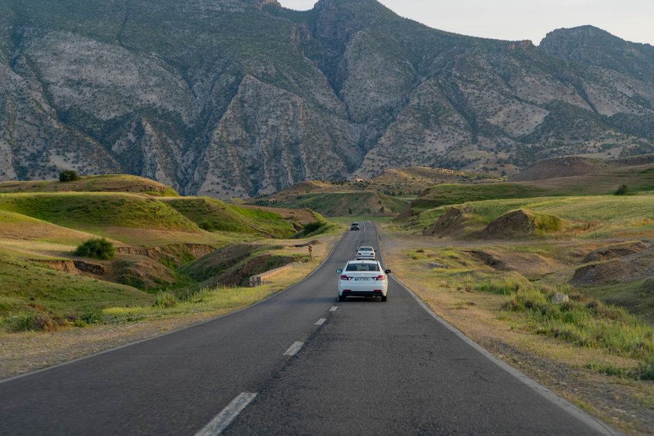 Picturesque view of a highway with cars surrounded by lush green hills and majestic mountains in summer.