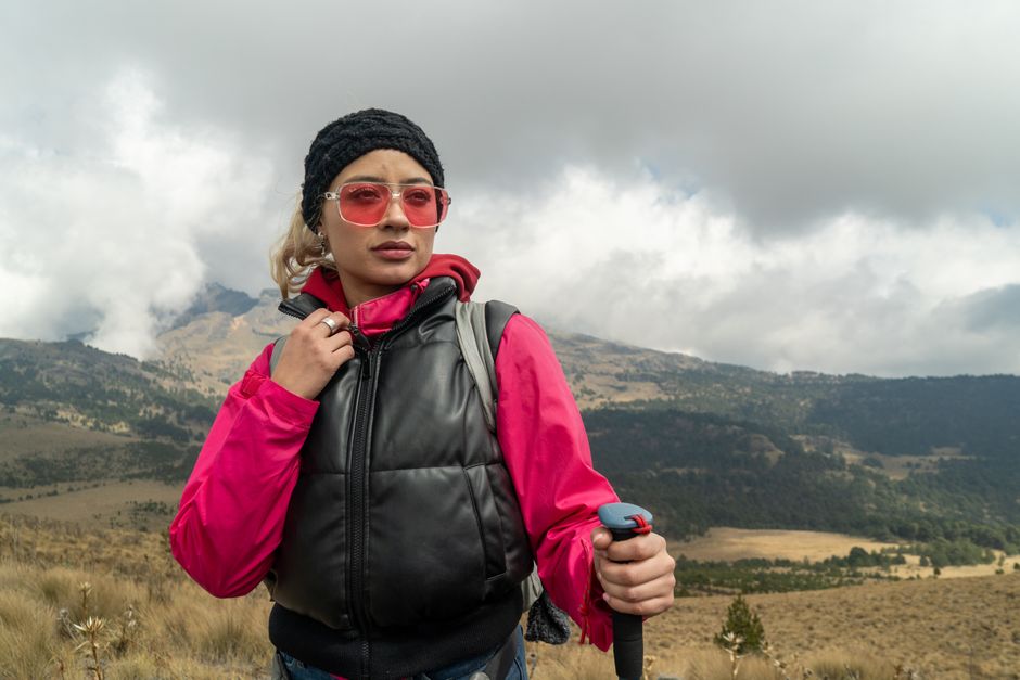 Woman in vibrant hiking gear explores a cloudy, mountainous landscape. Adventure awaits.