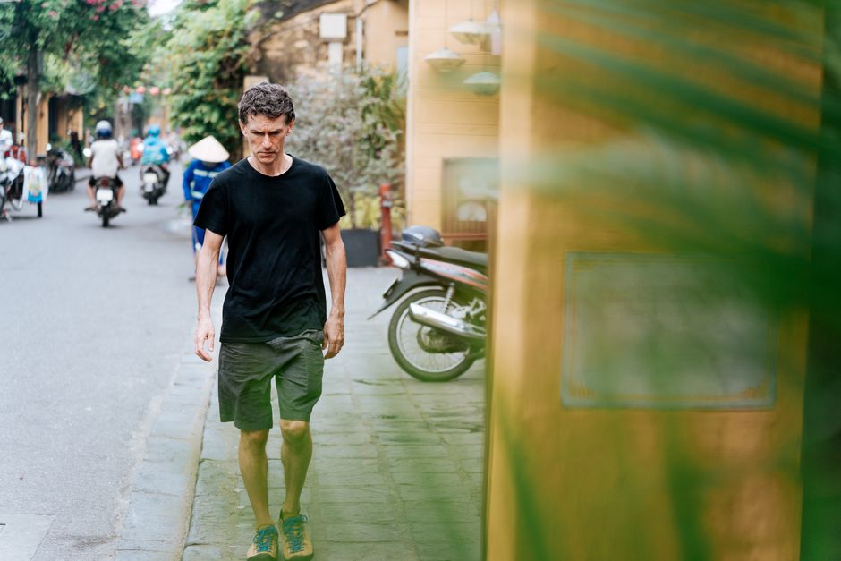 Man walking along a vibrant urban street with scooters in the background, embodying city life.