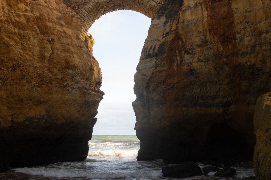 Breathtaking view of a natural arch formation on the Algarve coastline in Portugal, showcasing rugged cliffs and the Atlantic Ocean.