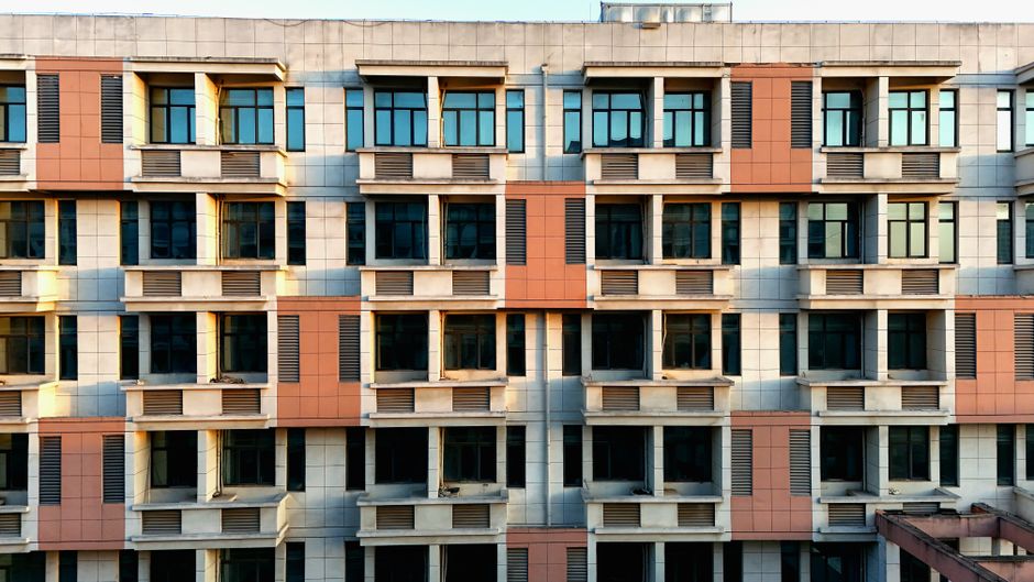 Front view of a modern, symmetrical apartment building with sunlight reflecting on windows.