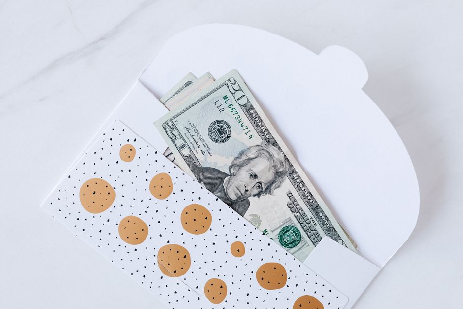 Top view of open carton money envelope with pile of paper money for birthday gift on white table