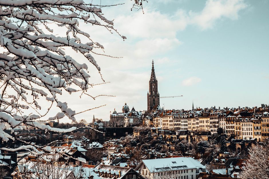 A scenic view of Bern, Switzerland with snow-covered rooftops and a historic cathedral under a winter sky.