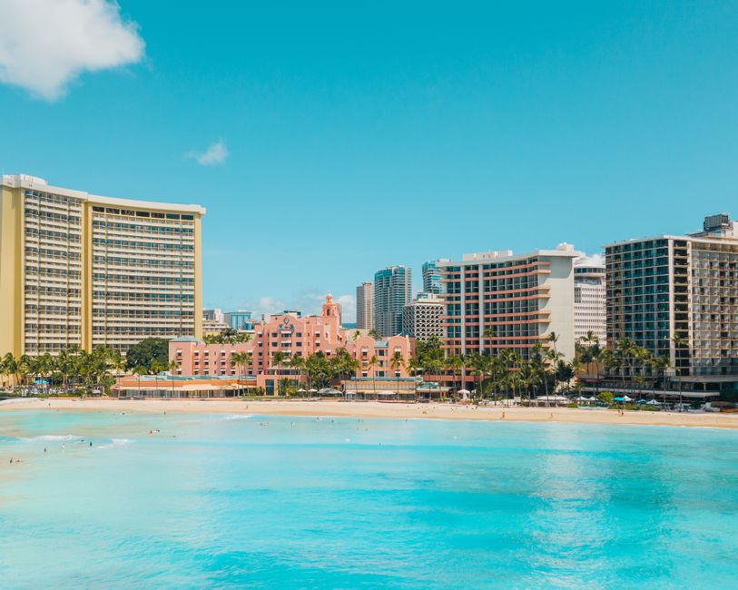 Aerial view of Waikiki's beachfront resorts and clear ocean waters under a bright blue sky.