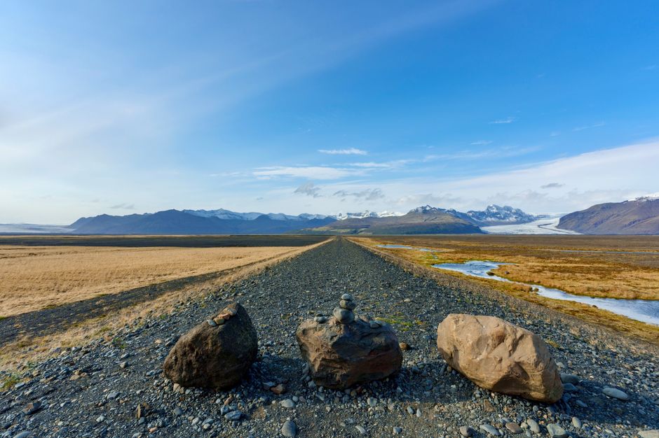A stunning view of a gravel road leading to distant mountains under a clear blue sky in Iceland.