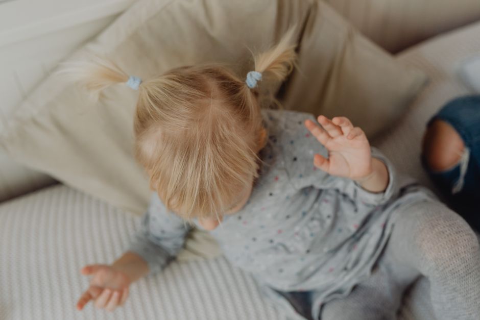 Sweet blonde-haired child in playful mood on a cozy sofa indoors.