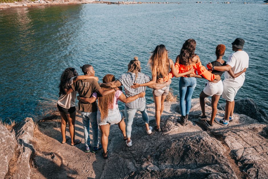 A group of friends standing on rocks, arms around each other, enjoying a scenic lake view.
