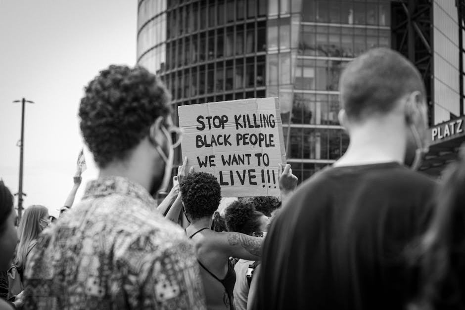 Protesters gather with placards demanding racial justice and equality in an urban setting.