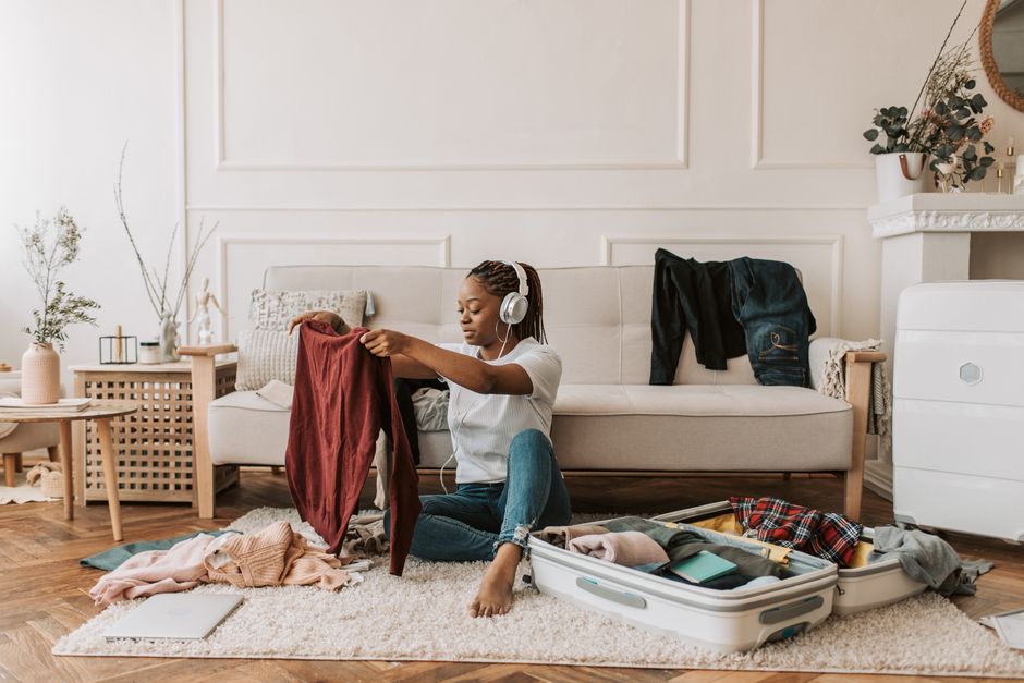 Woman preparing for travel at home, packing luggage, and listening to music.