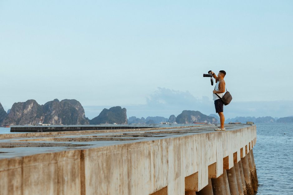 A photographer stands on a pier capturing scenic Ha Long Bay in Vietnam.