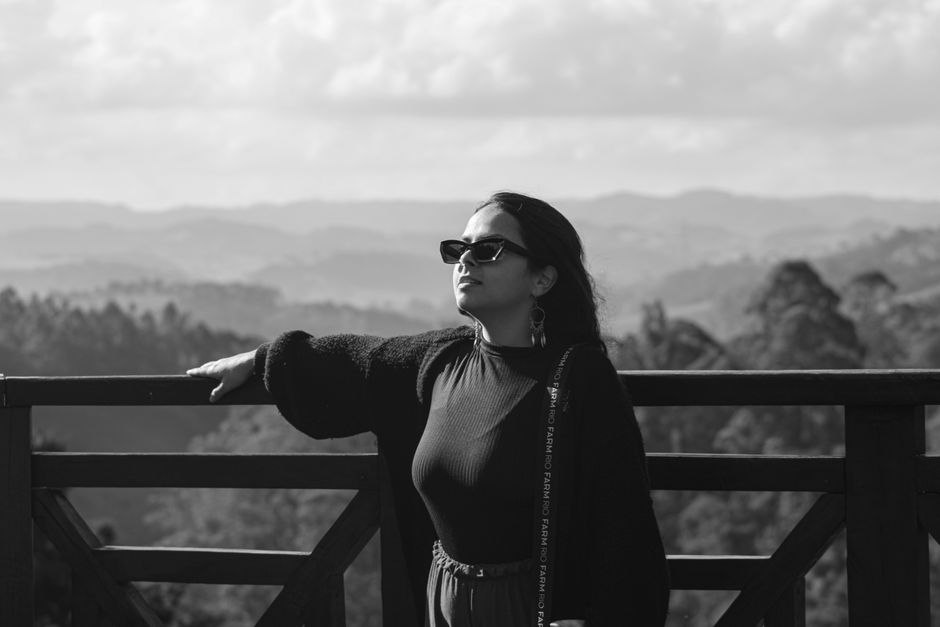 Woman in sunglasses enjoying a scenic mountain view on a sunny day, captured in black and white.