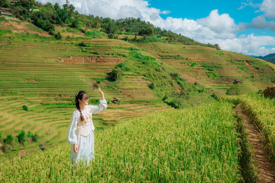 Asian woman smiling in traditional clothing on lush rice terraces, a vibrant representation of rural fashion and nature.