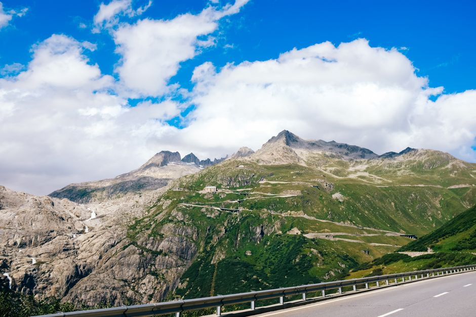 A stunning mountain road winding through lush green hills under a vibrant blue sky.