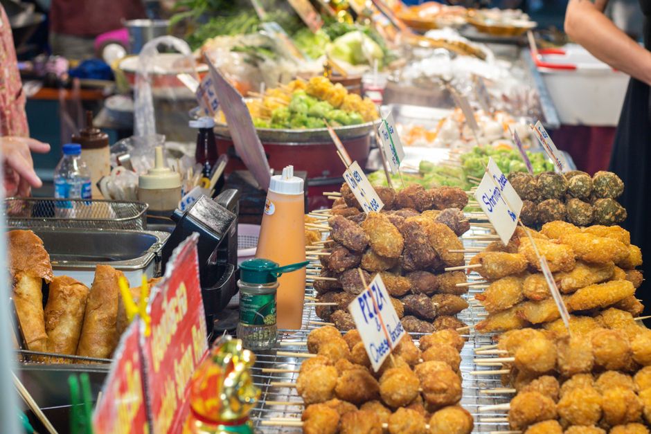A vibrant street food stall offering a variety of skewers and snacks in a busy market setting.