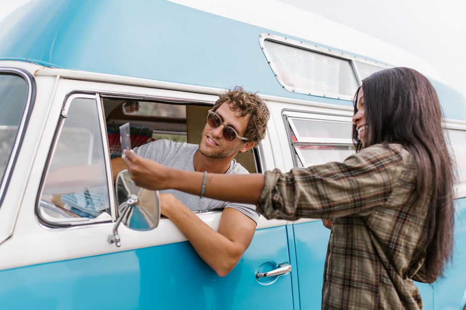 Happy couple on a road trip in a vintage blue camper van, embracing the van life spirit.