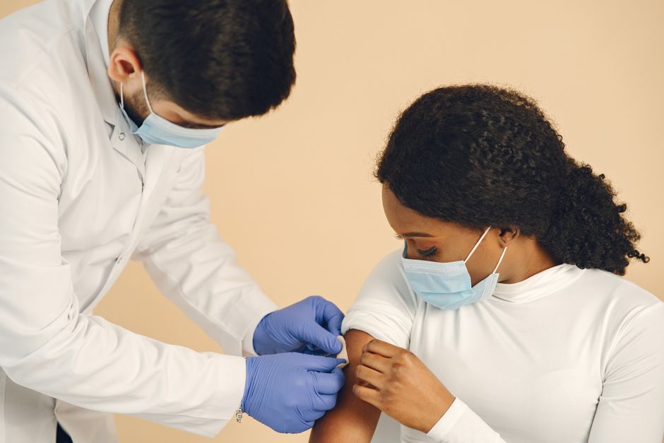 Medical professional in a mask giving a vaccine shot to a woman in a clinical setting.