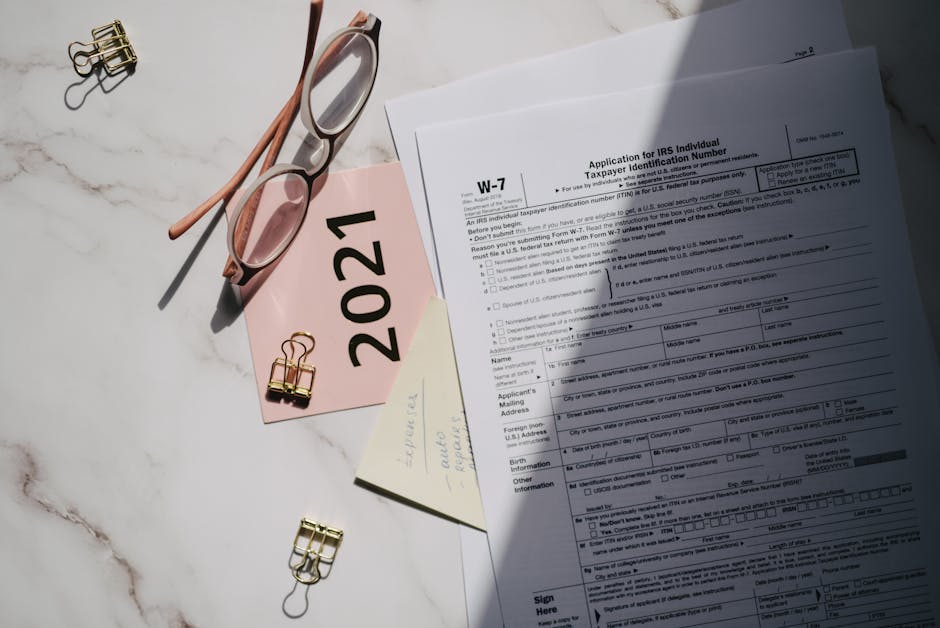 Flat lay of IRS tax documents with reading glasses and 2021 note on a marble surface.