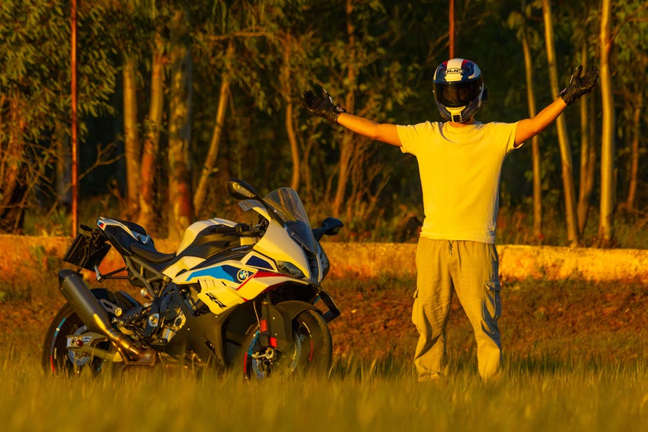 A motorcyclist in protective gear stands with arms wide open beside a sports bike during a beautiful sunset.