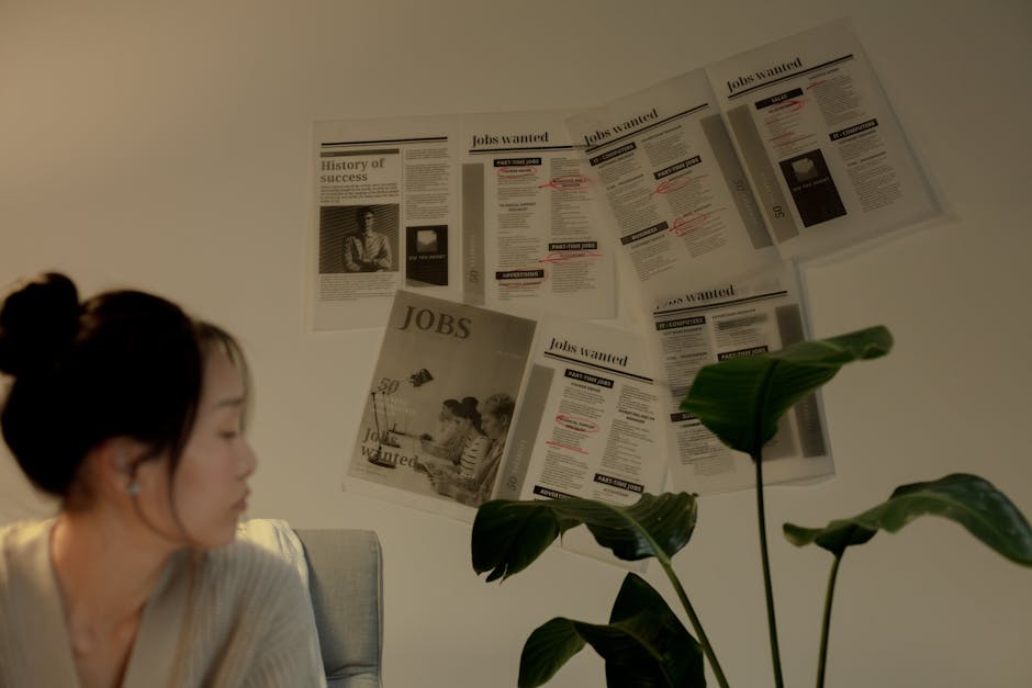 A woman sits pensively indoors beside a plant and job postings.